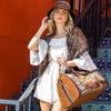 Woman in white jumpsuit, bucket hat and our duffel bag stylishly posing and showing off her Nicole Lee kimono in our Heaven on Earth design.
