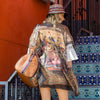 Woman in white jumpsuit, bucket hat and our duffel bag stylishly posing and showing off her Nicole Lee kimono in our Heaven on Earth design set on a contemporary background.