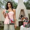 Model wearing a blush pink bustier top and light wash denim jeans outside in a picnic setting holding the Nicole Lee Violet Blossoms zip wallet and wearing the Violet Blossoms crossbody around her body while the backpack sits on a nearby picnic table amongst a bouquet of flowers. 
