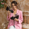 Women sitting in a wood bench wearing a pink blazer and blue jeans smiling, holding our Kali Espadrille Wedge sandal in black set in a modern background.