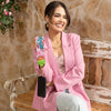 WOMEN IN A PINK BLAZER AND WHITE PANTS SITTING IN A VINTAGE BENCH HOLDING HER PHONE WITH OUR DETACHABLE WRISTLET STRAP.