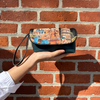 HOLDING OUR JENI MAKEUP BAG IN OUR NICOLE LEE MARTHA TRAVELS ITALY DESIGN SET ON A BRICK WALL.