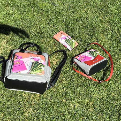 Outdoor lifestyle photo of the Nicole Lee vegan leather 3-in-1 Violet Blossom set set against a sunny grass day with a shadow hand reaching out for the large backpack. 