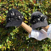 HOLDING OUR 2 CAPS IN OUR MIDNIGHT DESIGN SET IN A NATURE BACKROUND.